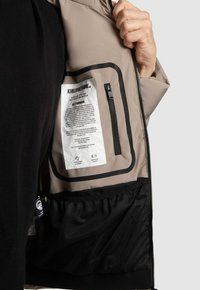 Beige jasseninterieur met zwarte accenten, voorzien van een ritszakje en een waslabel. Mesh zak aan de onderkant, gladde textuur.
