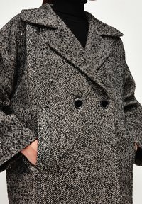 Wollmischung Hahnentrittmantel in Schwarz und Weiß, mit einem doppelt-knöpfbaren Design, großen Revers und Fronttaschen. Schwarze Knöpfe akzentuieren die Vorderseite.