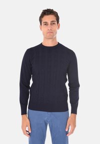 Maglione a trecce blu navy con scollo rotondo, maniche lunghe e polsini e orlo a coste. Il motivo testurizzato è ben evidente.