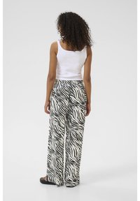 Pantaloni a gamba larga con stampa zebra bianco e nero abbinati a un top aderente bianco; il tessuto sembra leggero e morbido con una vita elastica.