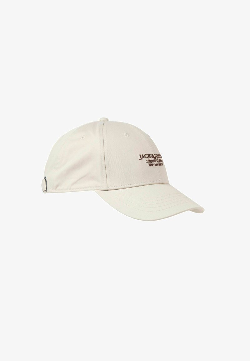 Beige cotton baseball cap with a curved brim, adjustable strap, and brown embroidered logo on the front. Textured fabric details visible.