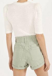 Top blanco de manga corta y textura peluda combinado con pantalones cortos de talle alto en verde claro, con cintura fruncida y dobladillo enrollado.