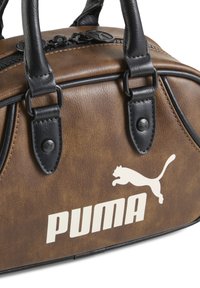 Hnedá kabelka z faux kože s čiernymi akcentmi, robustné uchá, zipsové zapínanie a biele logo Puma. Textúrovaný povrch so subtílnym leskom.