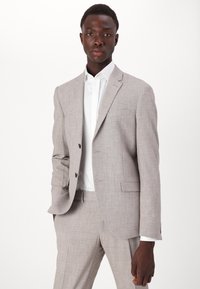 Fato cinza claro feito de tecido texturizado com um corte slim. Apresenta lapelas com recorte, fechamento de dois botões e uma camisa de vestir branca por baixo.