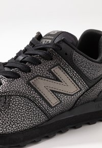 Schwarzer New Balance Sneaker mit strukturiertem Obermaterial, auffälligem grauem "N"-Logo und schwarzen Schnürsenkeln. Verfügt über einen gepolsterten Schaft und eine Gummisohle.