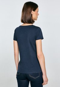 Navy modré tričko s krátkým rukávem, kulatým výstřihem, hladkým povrchem a přiléhavým střihem, z pohledu zezadu bez viditelných vzorů nebo kovových prvků.