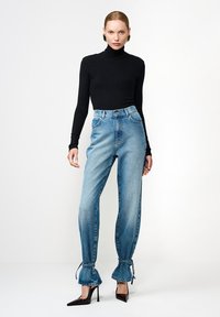 Bluză neagră cu mâneci lungi și guler înalt, asortată cu blugi din denim albastru deschis, cu talie înaltă, tivuri adunate și șnururi la gleznă, completată de pantofi negri cu toc.