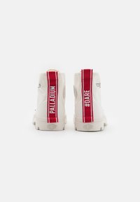 Baskets montantes blanches avec des tirants rayés rouges et blancs, un logo en relief et des semelles en caoutchouc texturé.