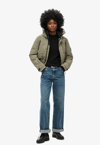 Oliwkowa pikowana kurtka z kapturem, w połączeniu z czarnym swetrem i jasnoniebieskimi dżinsami o prostym kroju. Czarne buty, podwinięte nogawki dżinsów.