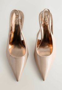 Zapatos slingback de charol color nude con punta estrecha y forro interior metálico dorado. Presentan un diseño recortado curvo en los laterales.