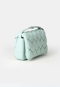 Miętowa skórzana torba o plecionym wzorze, zaokrąglonym kształcie i krótkim uchwycie. Posiada subtelne logo z boku, kompaktowy i elegancki design.