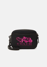 Černá kožená taška s texturovaným povrchem, na které se nachází růžový grafický design dinosaura a vozu, a řetězově zdobený popruh.