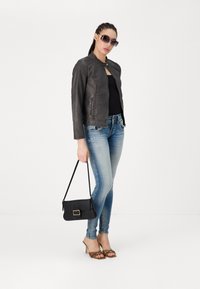 Chaqueta de cuero negra con un diseño ajustado, combinada con jeans skinny de mezclilla claros y desgastados. Accesorios incluyen un bolso negro y sandalias de tacón.