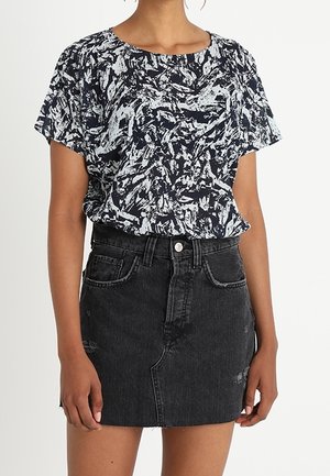 Kortärmad topp med ett marinblått och vitt abstrakt mönster, kombinerad med en svart denimkjol med hög midja och framfickor.