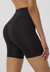 Shorts neri a vita alta realizzati in un tessuto liscio e elasticizzato, con un design senza cuciture e lunghezza a metà coscia, caratterizzati da una decorazione minima.