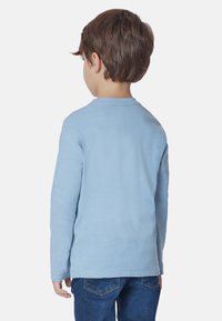 Camicia a maniche lunghe azzurro chiaro con collo tondo, realizzata in tessuto morbido, vista da dietro. Abbinata a jeans in denim blu.
