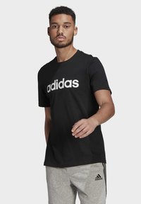 Musta lyhythihainen t-paita, joka on valmistettu puuvillasta ja jossa on suuri valkoinen "adidas"-logo edessä. Suunnittelu on klassinen ja yksinkertainen.