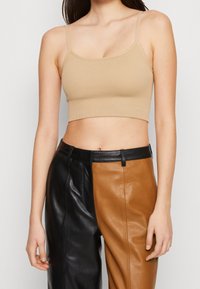 Beige ribbat crop top med tunna band, med en figurnära design. Sammanfattad med färgad läderbyxor i svart och brunt.