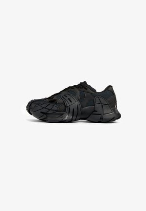 Zapatillas deportivas negras con parte superior de malla, suela de goma texturizada, diseño moldeado único y sistema de cordones integrado para un ajuste seguro.
