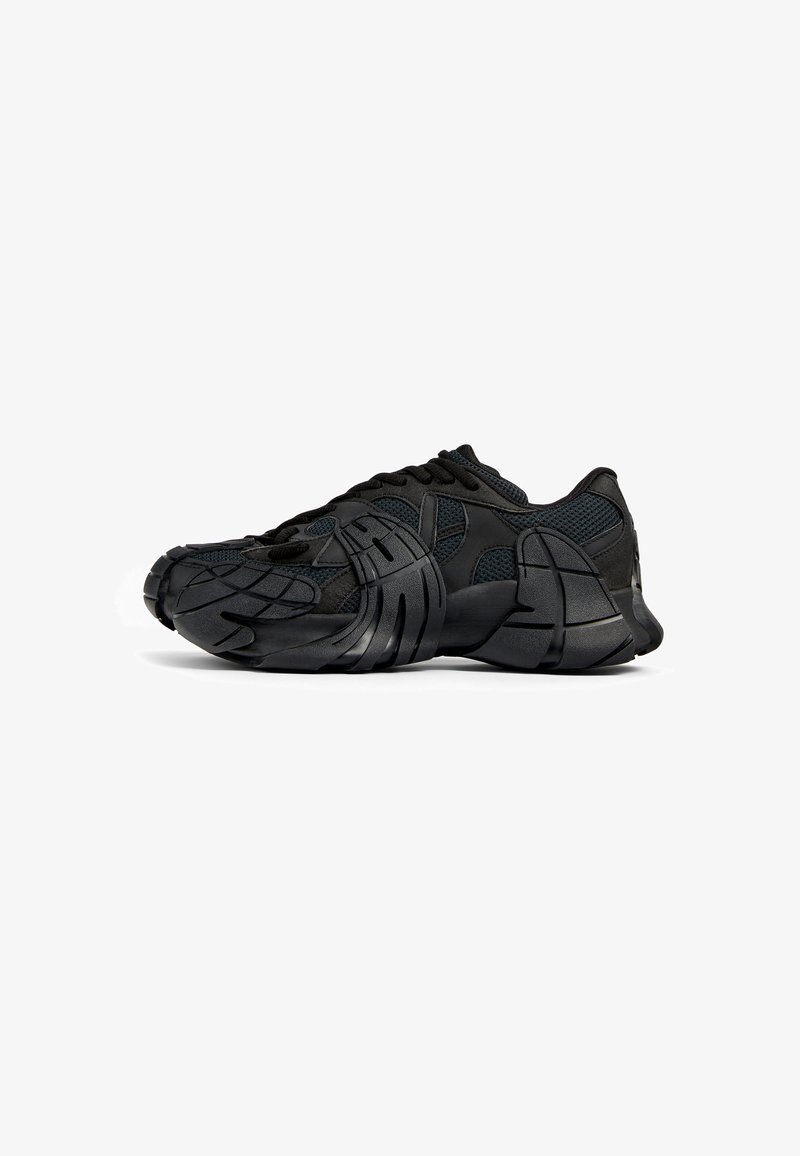 Zapatillas deportivas negras con parte superior de malla, suela de goma texturizada, diseño moldeado único y sistema de cordones integrado para un ajuste seguro.