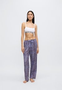 Hvid sports-bh med sort bånd, kombineret med løstsiddende lilla bukser med leopardprint og bindebånd i taljen.