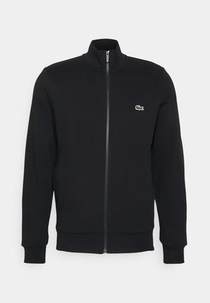 Manche et torse d'un sweat-shirt noir montrant une poche zippée partiellement ouverte sur le côté avec des poignets et un ourlet côtelés.