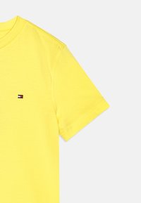 Žluté bavlněné tričko s kulatým výstřihem a krátkými rukávy. Na hrudi má malé trojbarevné logo. Hladký materiál a uvolněný střih.