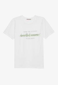 Vit bomullströja med korta ärmar, med grön och svart text som säger "Det finns så många vackra anledningar att vara lycklig."