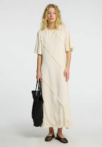 Vestido de color crema claro con mangas cortas, con costuras diagonales texturizadas. Combinado con un bolso negro de tejido y unos zapatos slip-on de malla.