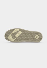 Semelle de chaussure avec motif hexagonal et grips beiges géométriques sur fond gris, montrant le logo de la marque près du talon.