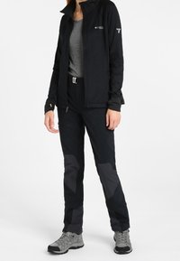 Svart fleecejacka med dragkedja, grå skjorta och svarta byxor med grå detaljer. Vattentäta grå vandringsskor fulländar outfiten.