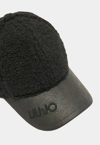 Must mustaga pealmise tekstuuriga villast ja läikiva nahkst brimiga. Esipaneelil on reljeefselt toodud logo "LIU JO".