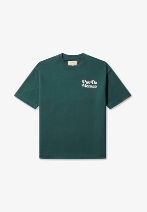 Zeleni pamučni majica kratkih rukava. Na prednjem lijevom dijelu ima bijeli natpis "Pas De Monaco". Okrugli izrez, opušteni kroj.