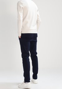 Felpa chiara, pantaloni blu navy, design aderente. Sneaker bianche con accenti. Texture liscia, stile casual, vista da dietro.