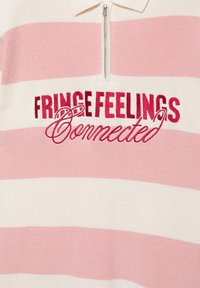 Pull en maille à col avec des rayures horizontales roses et blanches, fermeture éclair avant et texte rouge brodé "FRINGE FEELINGS Connected."