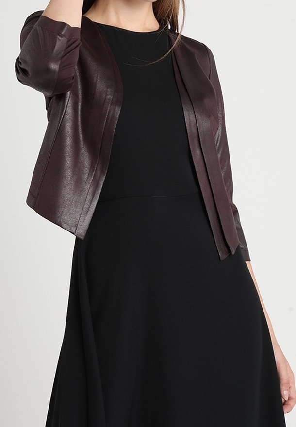 Veste bordeaux cintrée avec manches trois-quarts, fabriquée en matériau brillant, conçue pour être portée sur une robe noire. Texture lisse, devant ouvert.