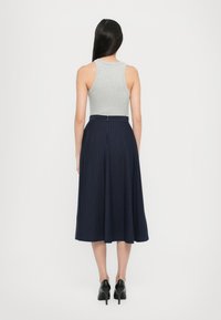 Rückansicht einer Person in einem enganliegenden grauen Tanktop und einem marineblauen Midirock mit vertikalen Streifen. Der Rock hat einen Bund und einen Reißverschluss.