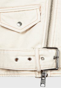 Dettaglio di una giacca di jeans bianca con cerniera argentata, bottoni a pressione in metallo e vita con cintura dotata di occhielli e accenti di cuciture arancioni.