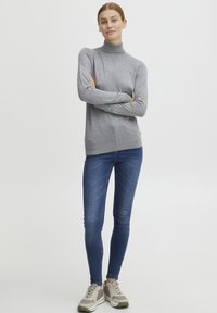 Szürke garbó pulóver puha anyagból, kék skinny farmernadrággal és világosszürke sportcipővel párosítva. Egyszerű design, látható minták nélkül.