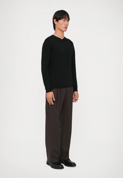 Pull de malha canelada preto de manga longa com decote em V, combinado com calças largas castanho-escuras e sapatos pretos; design minimalista.