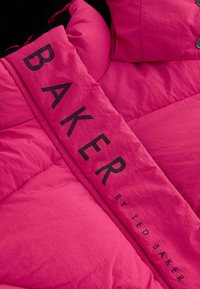 Rozā izklāta jaka ar izteiksmīgu melnu uzrakstu "BAKER" un "by TED BAKER", ar gludu tekstūru un noapaļotiem dizaina elementiem.
