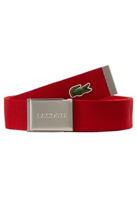 Ceinture en tissu rouge avec une boucle en métal argenté gravée "LACOSTE" et un logo crocodile vert cousu sur la lanière.