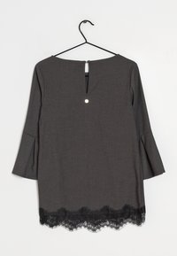 Abito grigio con maniche a palloncino, dotato di un piccolo scollo a chiave sul retro e orlato con pizzo nero lungo l'orlo inferiore. Tessuto morbido.