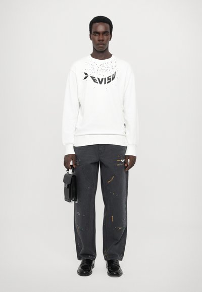 Hvid sweatshirt med sort skrift, parret med løse grå jeans med malerpletter og en sort taske. Sorte sko fuldender looket.