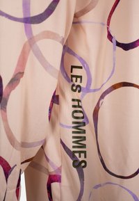 Blush stof met abstracte paarse en rode cirkelpatronen; voorzien van de tekst "LES HOMMES" in het groen op de zijkant. Zachte textuur en een gladde afwerking.