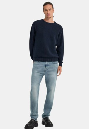 Maglione lavorato a maglia di un blu navy scuro con un motivo testurizzato, abbinato a jeans azzurri chiari e scarpe nere stringate. Design semplice e vestibilità rilassata.