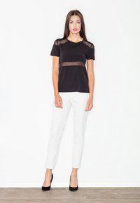 Czarna koszulka z prześwitującymi panelami z siateczki na ramionach i w talii, zestawiona z białymi, dopasowanymi spodniami i czarnymi szpilkami, na jasnym tle.