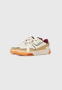 Witte en beige sneakers van gemengde materialen met geperforeerde accenten, een kastanjebruine kraag en een oranje zool; voorzien van veters en een logo details aan de zijkant.