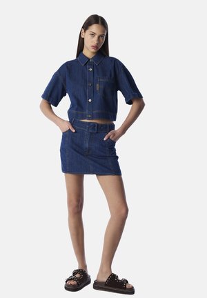 Denim crop shirt met korte mouwen, knoopsluiting, voorkruiszak, gecombineerd met een high-waisted denim rok. Zwarte platformsandalen met versieringen.