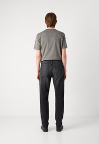 Camiseta gris de algodón y jeans de mezclilla negros, con un diseño de pierna recta y detalles en el bolsillo trasero, situados sobre un fondo neutro.